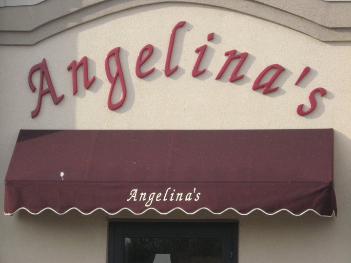 Red script letters spelling "Angelina's" on a beige wall above a maroon awning, which also has "Angelina’s Restaurant" in white script. A black-framed doorway is partially visible beneath the awning, inviting you to enjoy classic Italian food.