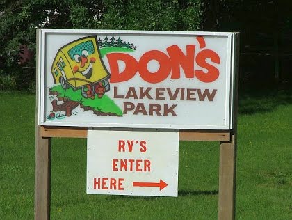 A sign reading "Don's Lakeview Park" with a cartoon cabin, and below, a smaller sign with an arrow saying "RV's Enter Here" points the way to RV camping at Lakeview RV Park on a grassy background.