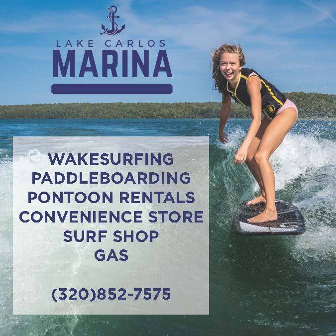 A young woman wakesurfs on a lake surrounded by trees near Alexandria, MN. Lake Carlos Marina offers lake country family fun with wakesurfing, paddleboarding, pontoon rentals, a store, surf shop, gas, and a phone number.