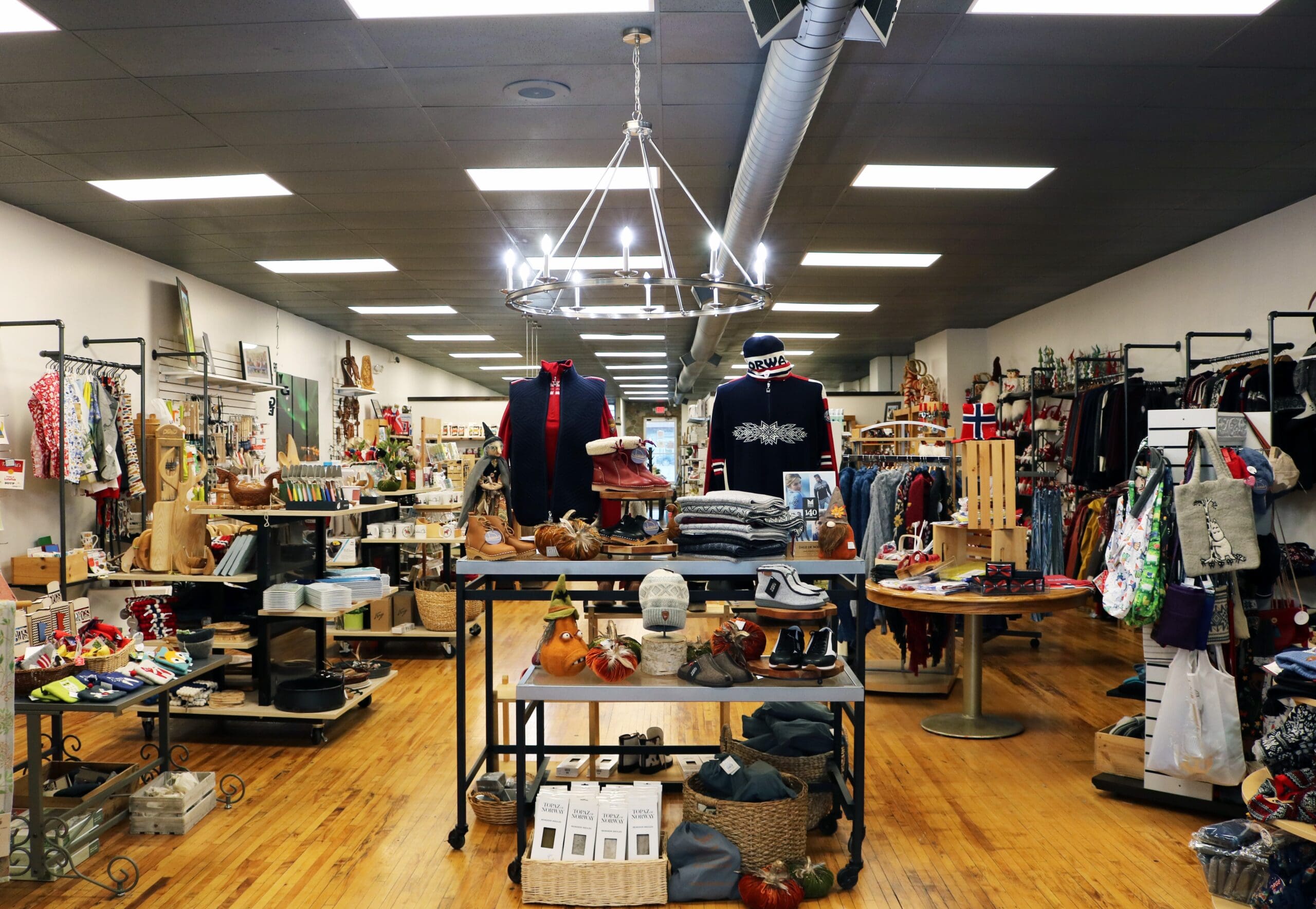 A boutique shop interior with wooden floors, display tables of clothes and accessories, and colorful racks—perfect for discovering new finds during spring in Alexandria or while exploring things to do in Alexandria.