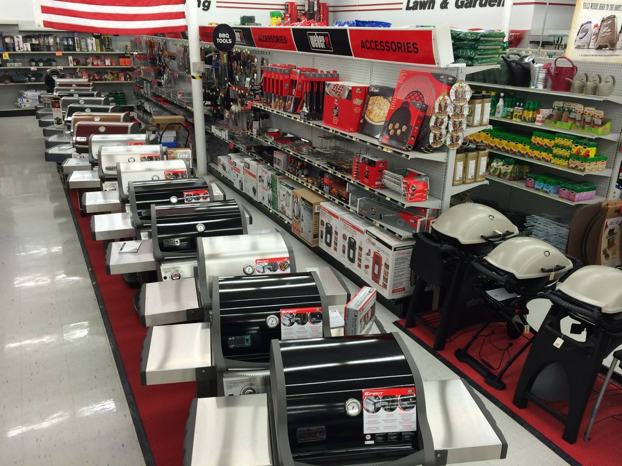 A store aisle at Ace Hardware displays various grills in the foreground, with shelves of grilling accessories, tools, and lawn and garden products in the background. The section is well-lit and organized—perfect for your next visit to an Ace Hardware store near me.
