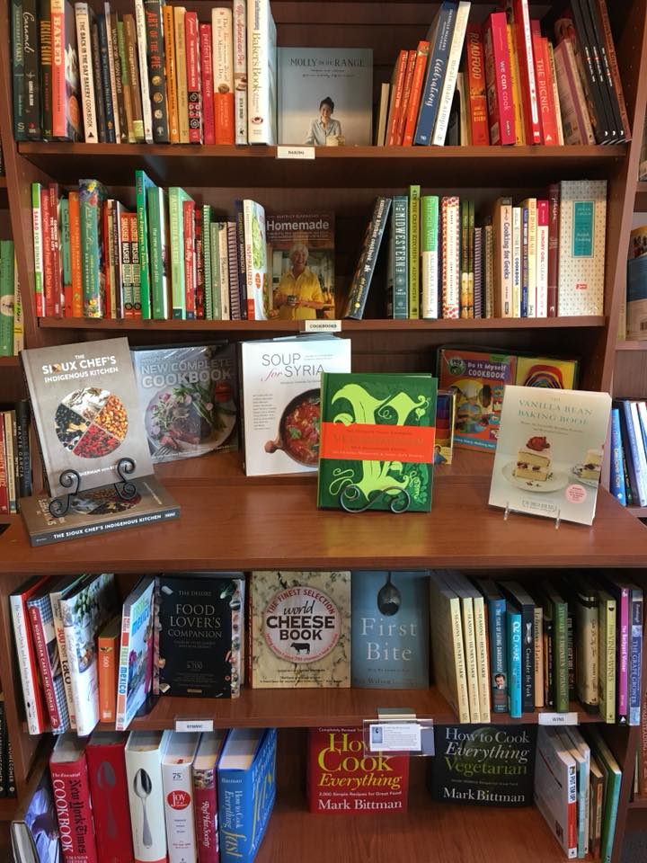 A Cherry Street Books display features shelves filled with colorful cookbooks, including several prominently displayed titles about soup, cheese, and Syrian cuisine, with a variety of other culinary books neatly arranged.