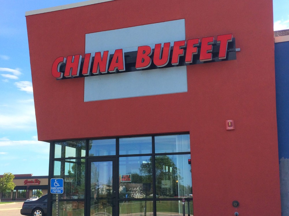 A red building with large windows displays a bright "China Buffet" sign near the entrance, where a blue handicap parking sign stands. The glass reflects nearby trees and other buildings.