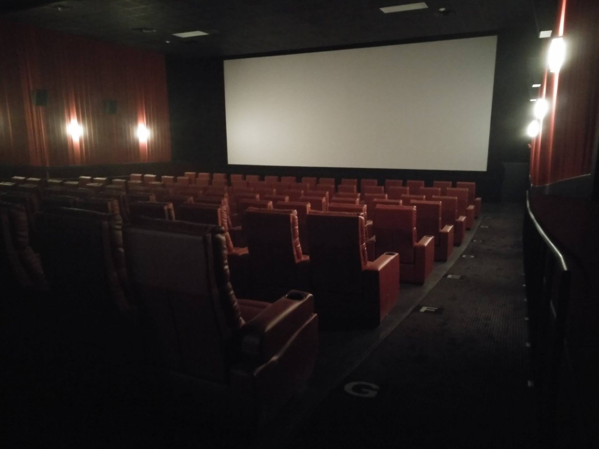A dimly lit Cinema 9 theater with rows of empty red leather seats faces a large blank screen, softly illuminated by wall lights along the side walls.