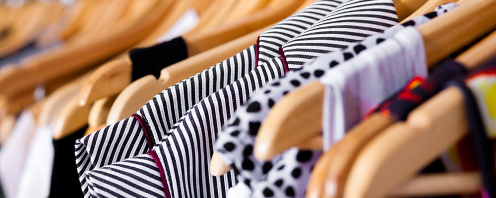 A close-up view of clothes hanging on wooden hangers in the Klothes Kloset, featuring various black and white patterns such as stripes and polka dots.