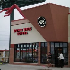 A Dunn Bros. Coffee shop with a drive-thru sign, large windows, and two people near the entrance. The red inflatable air dancer on the roof adds excitement to this inviting Dunn Bros. Coffee location.
