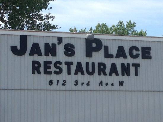 The sign for Jan’s Place Restaurant displays bold black letters on a light-colored building, with “612 3rd Ave W” written below Jan’s Place. Trees and blue sky can be seen in the background.