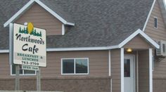 Northwoods Cafe is a brown building with white trim, featuring a peaked roof and visible windows and door. Out front, a sign reads "Northwoods Cafe, Breakfast & Lunches, 763-2900," welcoming guests inside.