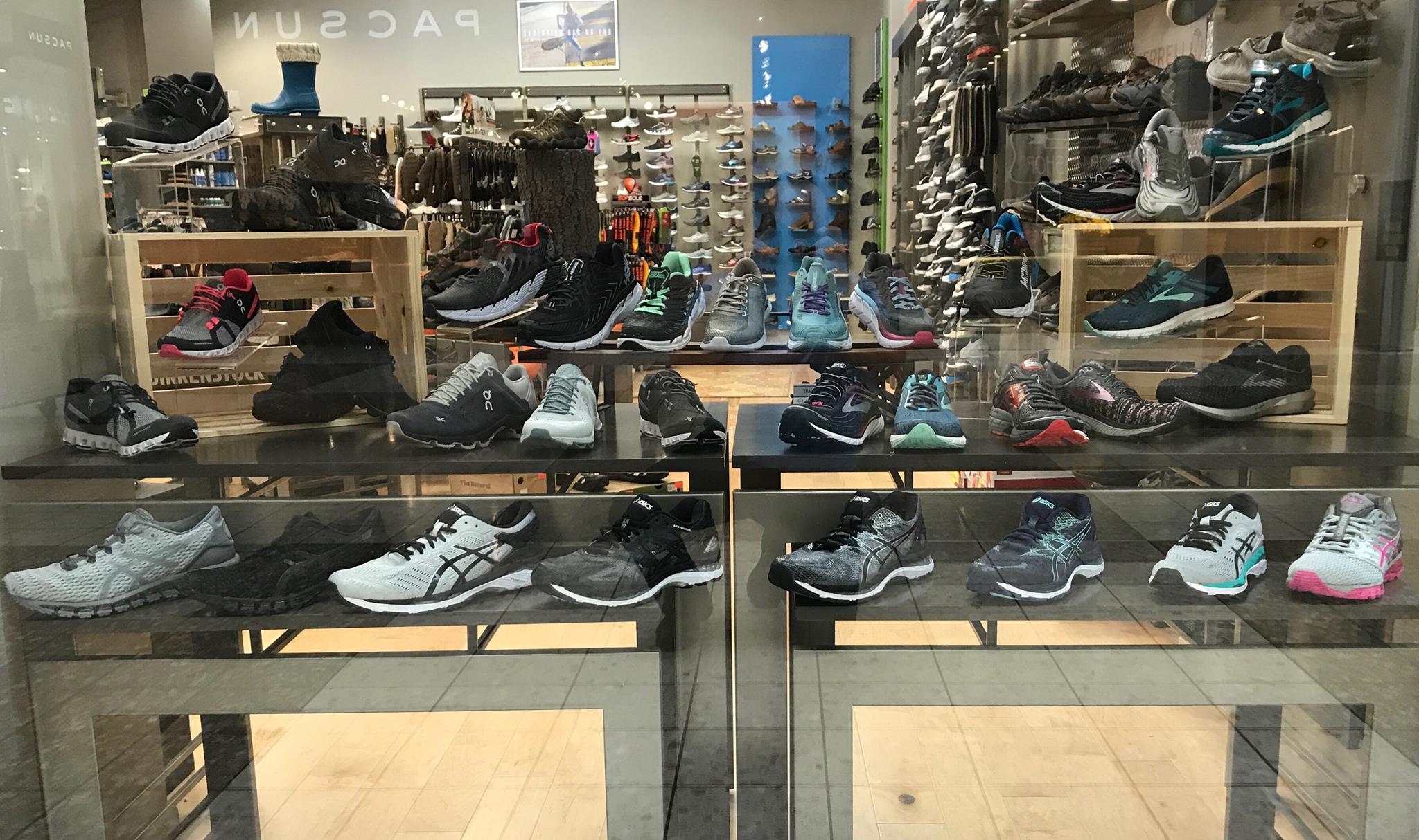 A store display for Tradehome Shoes showcases a variety of athletic shoes in different styles and colors, arranged on shelves and platforms behind a glass window. The background features even more shoes and store fixtures.