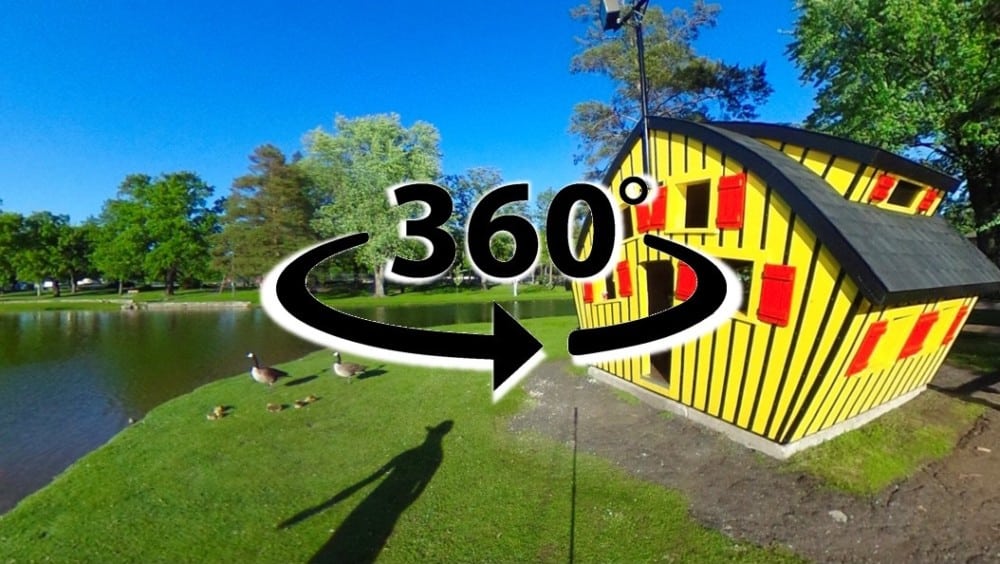 A vibrant yellow house with red shutters stands near a pond, surrounded by green grass, trees, and geese. A large “360°” symbol invites you to tale a 360 virtual tour of the Alexandria Lakes Area—discover more with Alexandria MN tourism.