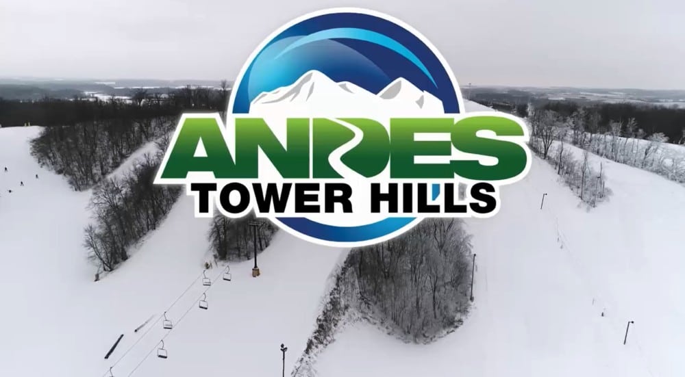 Logo for Andes Tower Hills featuring snowy mountains and stylized text, overlaid on a winter landscape with snow-covered hills, ski lifts, and trees—highlighting the excitement of skiing adventures in the background.