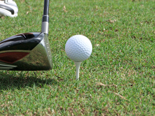 A close-up of a golf club positioned next to a white golf ball on a tee, ready for a shot on green grass—perfect inspiration for your next Autumn Golf Get-Away.