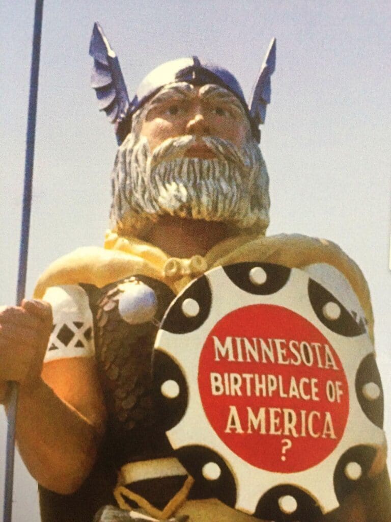 Statue of Big Ole, a Viking with a helmet and shield reading “Minnesota Birthplace of America?” The Viking has a blonde beard, wears armor, and stands proudly under a clear sky—perfect for celebrating his happy 50th birthday.