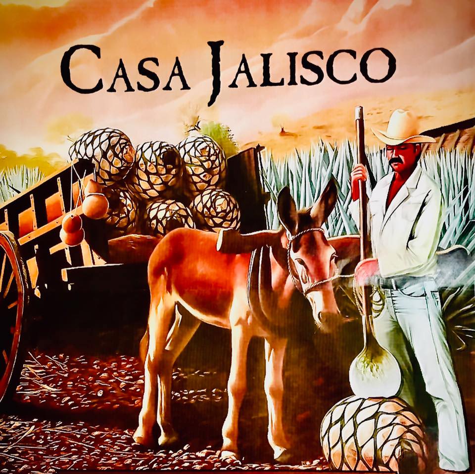 A man in a white suit and hat stands beside a brown donkey, holding a large agave heart. Behind them, a wooden cart is filled with agave piñas. At the top, "Casa Jalisco" highlights the traditional scene.