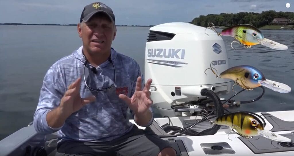 A man sits on a boat in front of a Suzuki 300 outboard motor, gesturing with his hands. Three colorful fishing lures are digitally added to the right side of the image, appearing to float in the air, highlighting his passion for fishing.