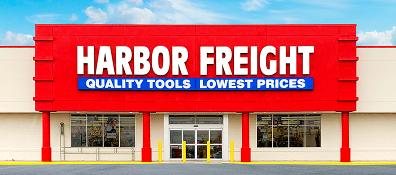The front of a Harbor Freight store features bold red Harbor Freight signage and a blue banner stating "Quality Tools Lowest Prices" above the main entrance.