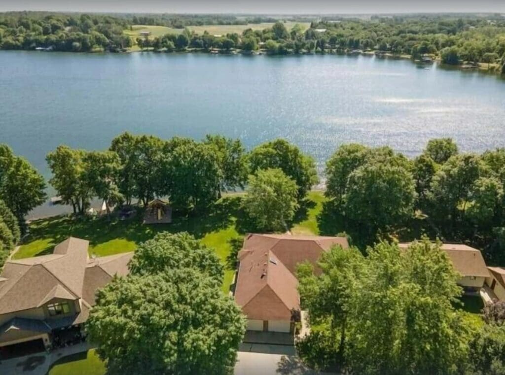 Aerial view of houses and tree-lined yards along the edge of calm Lake Latoka, with open green fields and wooded areas in the background under a clear sky—perfect for a peaceful family retreat.