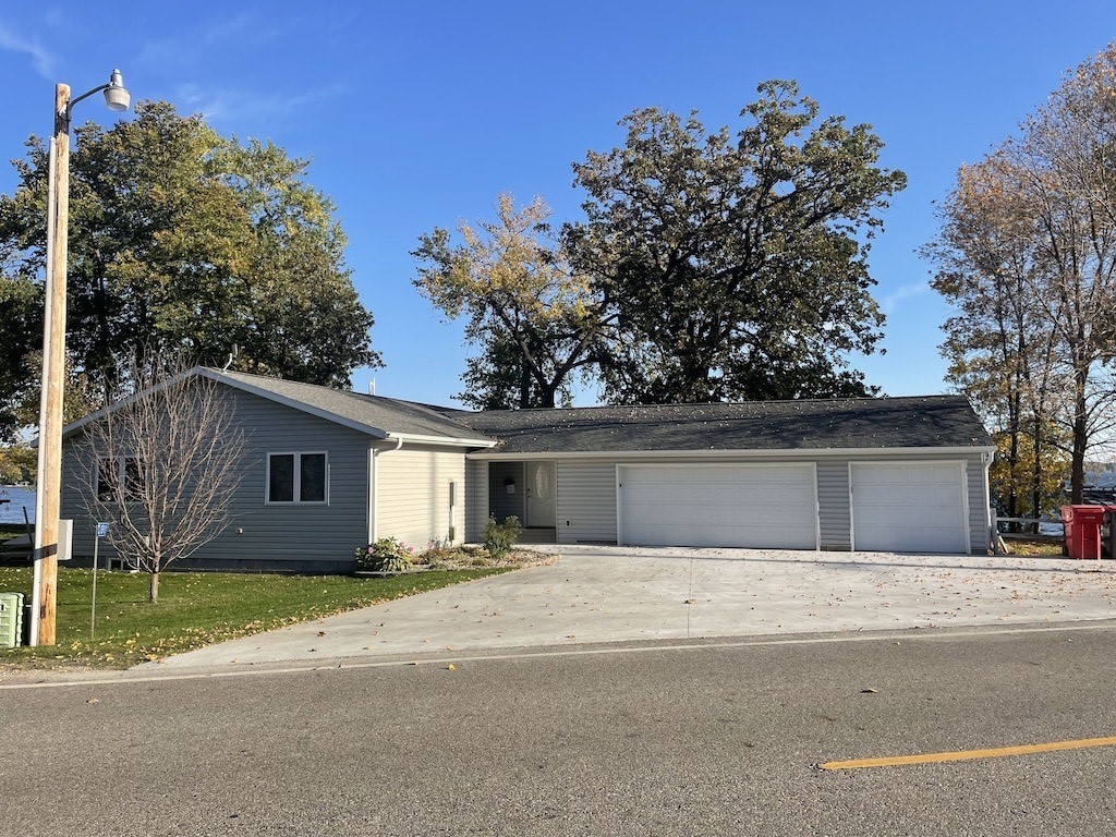 Single-story Private Vacation Home with light-colored siding, a spacious three-car garage, and a wide concrete driveway. The yard features trees, while the house is set against taller trees under a clear blue sky.