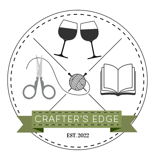 A circular logo with a dotted border featuring wine glasses, scissors, yarn, and an open book. A green ribbon displays “Crafters Edge,” while the text below reads “EST. 2022.” Perfect for creative gatherings at Crafters Edge.