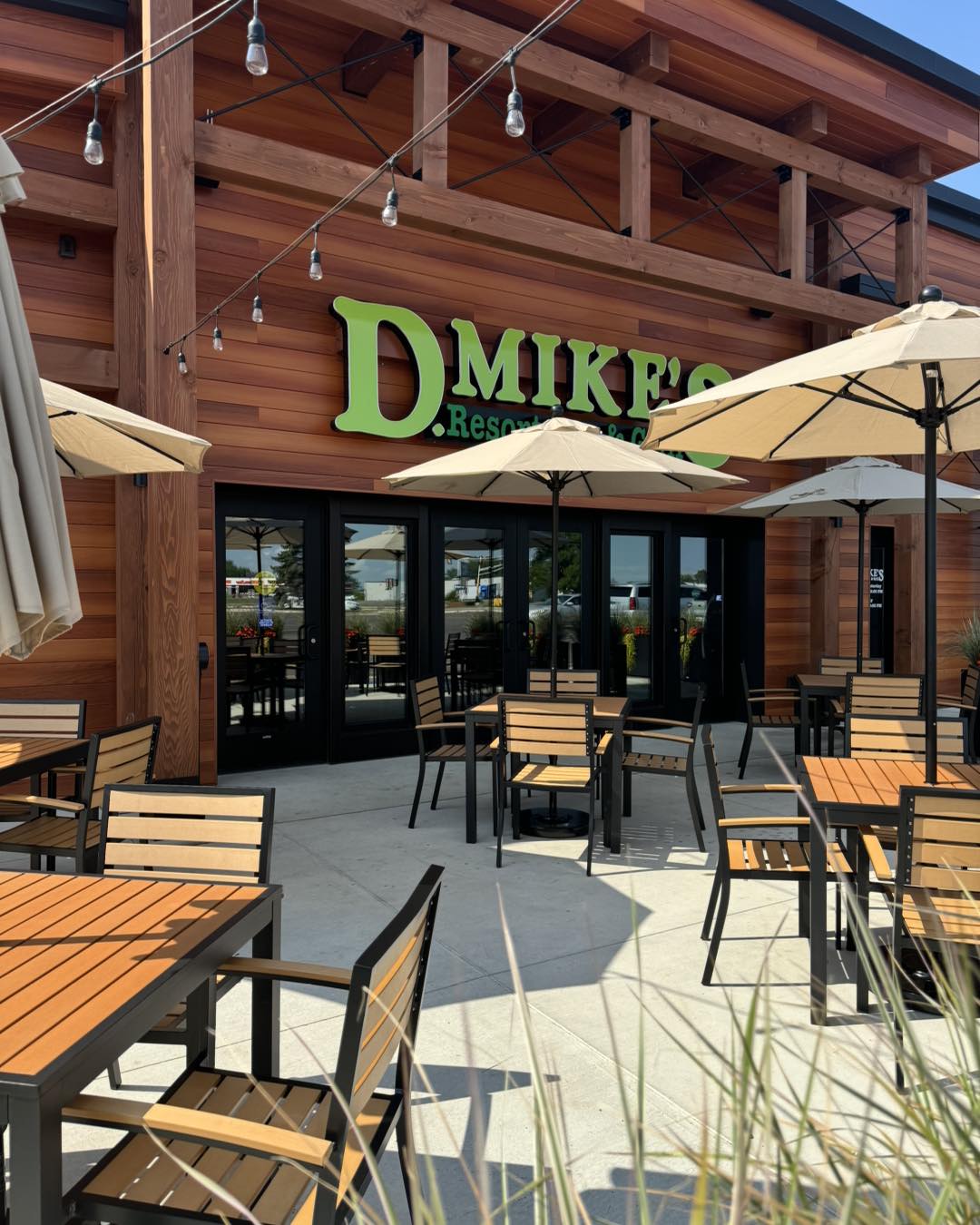 Outdoor patio of D. Mike’s Resort Bar & Grill, featuring wooden tables and chairs with umbrellas. The building’s wooden exterior and string lights overhead create a welcoming, casual dining atmosphere.