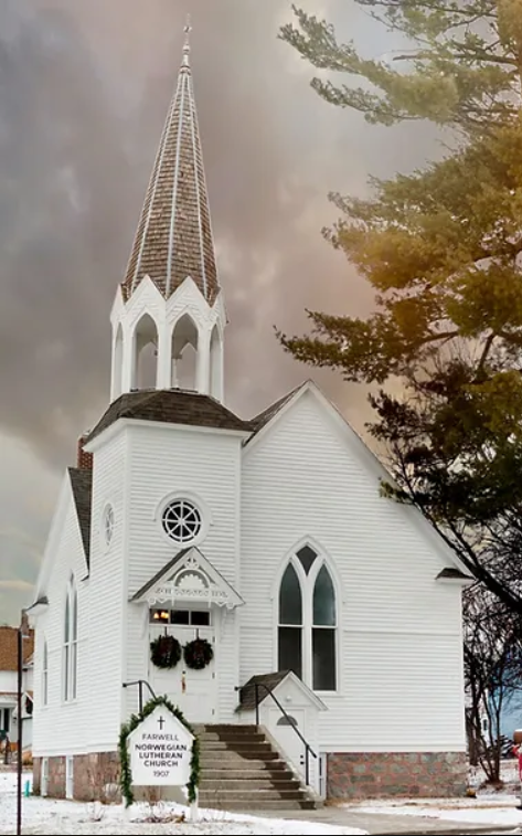 A white wooden Farwell Historic Church with a tall steeple and arched windows stands under a dramatic cloudy sky. A wreath-adorned sign in front reads "Raswell Norwegian Cemetery 1907." Snow covers the ground and trees frame the scene.