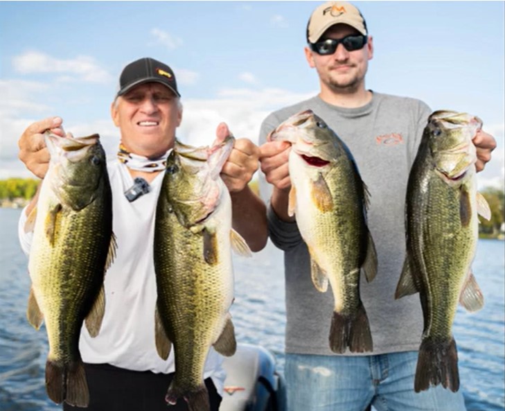 Two men standing outdoors on a boat, each holding up two large bass caught with crankbaits, smiling at the camera, with a lake and blue sky in the background.