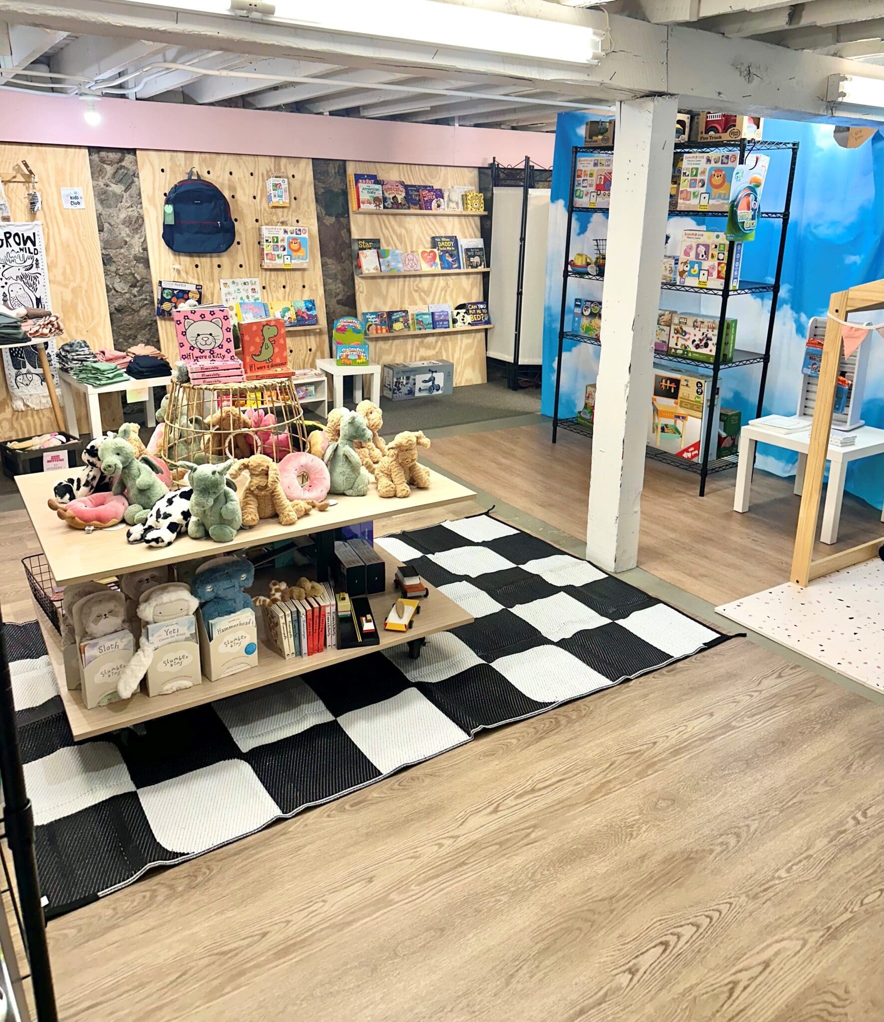 A cozy children’s shop, Lulie Boutique offers plush toys, books, and games on charming shelves and tables. With wood flooring, a checkered rug, and colorful decor, the space creates a playful and inviting atmosphere.