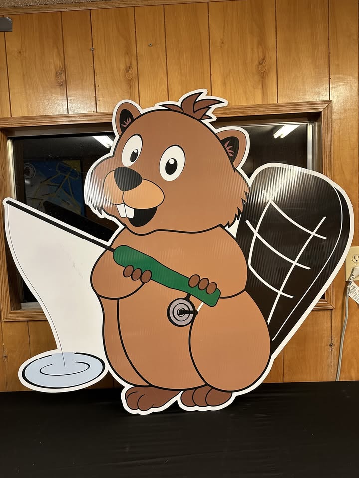 A large cartoon beaver cutout holds a green hose pouring water onto the floor, promoting the Annual Beaver Classic. The beaver stands against a wood-paneled wall with a window and electrical outlet in the background.