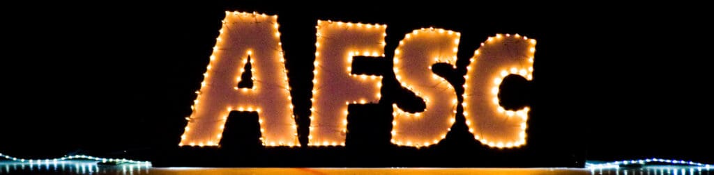 Large letters "AFSC" outlined with bright string lights stand against a dark background, capturing the excitement of the Annual Spring Ice Review, with additional lights glowing at the bottom edges of the image.