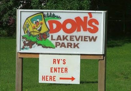A sign reading "Don's Lakeview Park" with a cartoon cabin, and below, a smaller sign with an arrow saying "RV's Enter Here" points the way to RV camping at Lakeview RV Park on a grassy background.