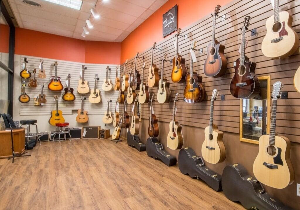 At Carlson's Music Center, a wall displays a variety of acoustic guitars, each hanging neatly on hooks. Guitar cases line the floor below, and the room features wood flooring and an orange accent wall.