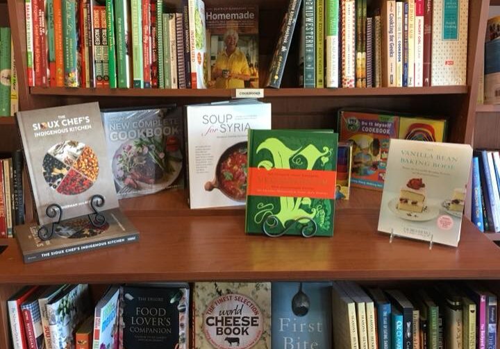 A Cherry Street Books display features shelves filled with colorful cookbooks, including several prominently displayed titles about soup, cheese, and Syrian cuisine, with a variety of other culinary books neatly arranged.