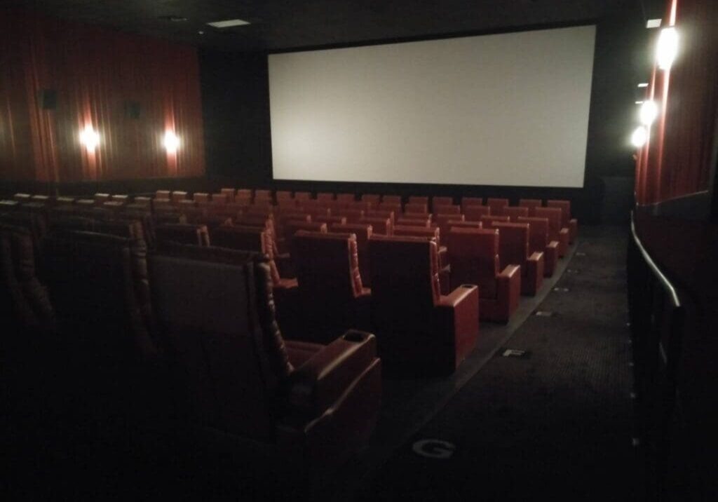 A dimly lit Cinema 9 theater with rows of empty red leather seats faces a large blank screen, softly illuminated by wall lights along the side walls.