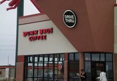 A Dunn Bros. Coffee shop with a drive-thru sign, large windows, and two people near the entrance. The red inflatable air dancer on the roof adds excitement to this inviting Dunn Bros. Coffee location.