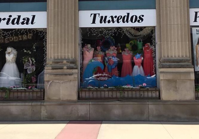 Jackie J's storefront features three large windows displaying bridal gowns, tuxedos, and prom dresses. Signs above each window read "Bridal," "Tuxedos," and "Prom." A poster of a couple in formalwear accents the prom window.