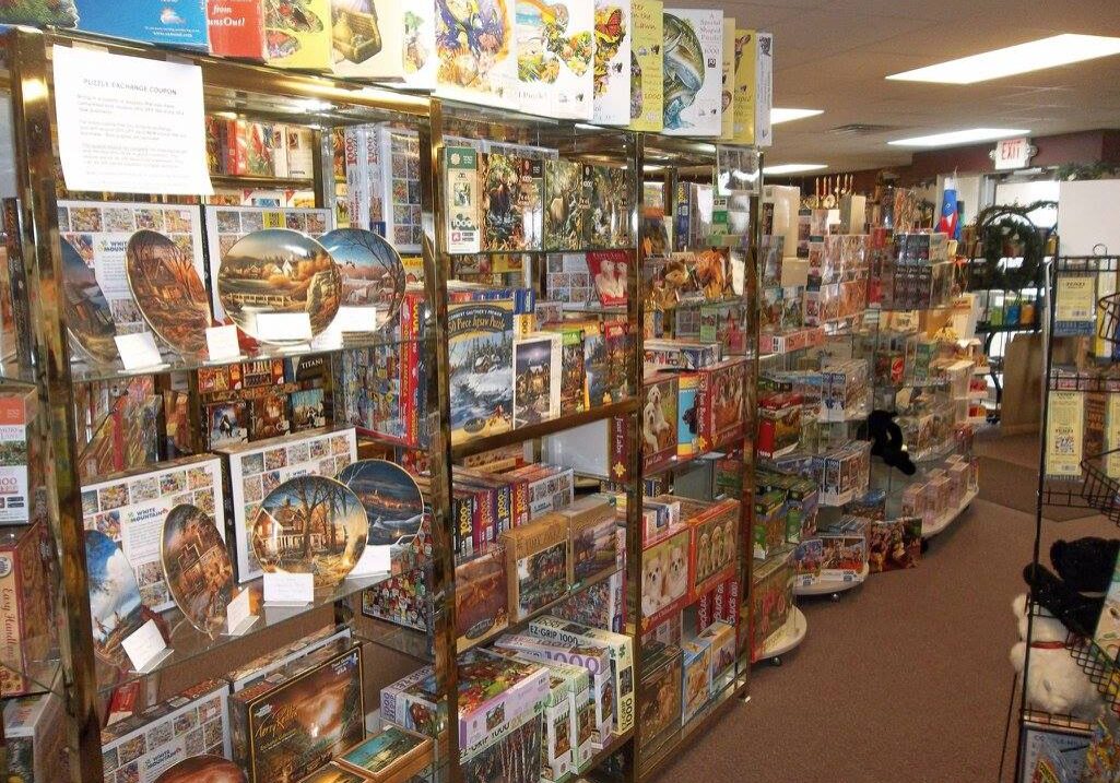 A store aisle filled with colorful puzzle boxes and board games neatly arranged on shelves, inviting families to create special memories together, with some puzzles on display and stuffed animals visible in the background.